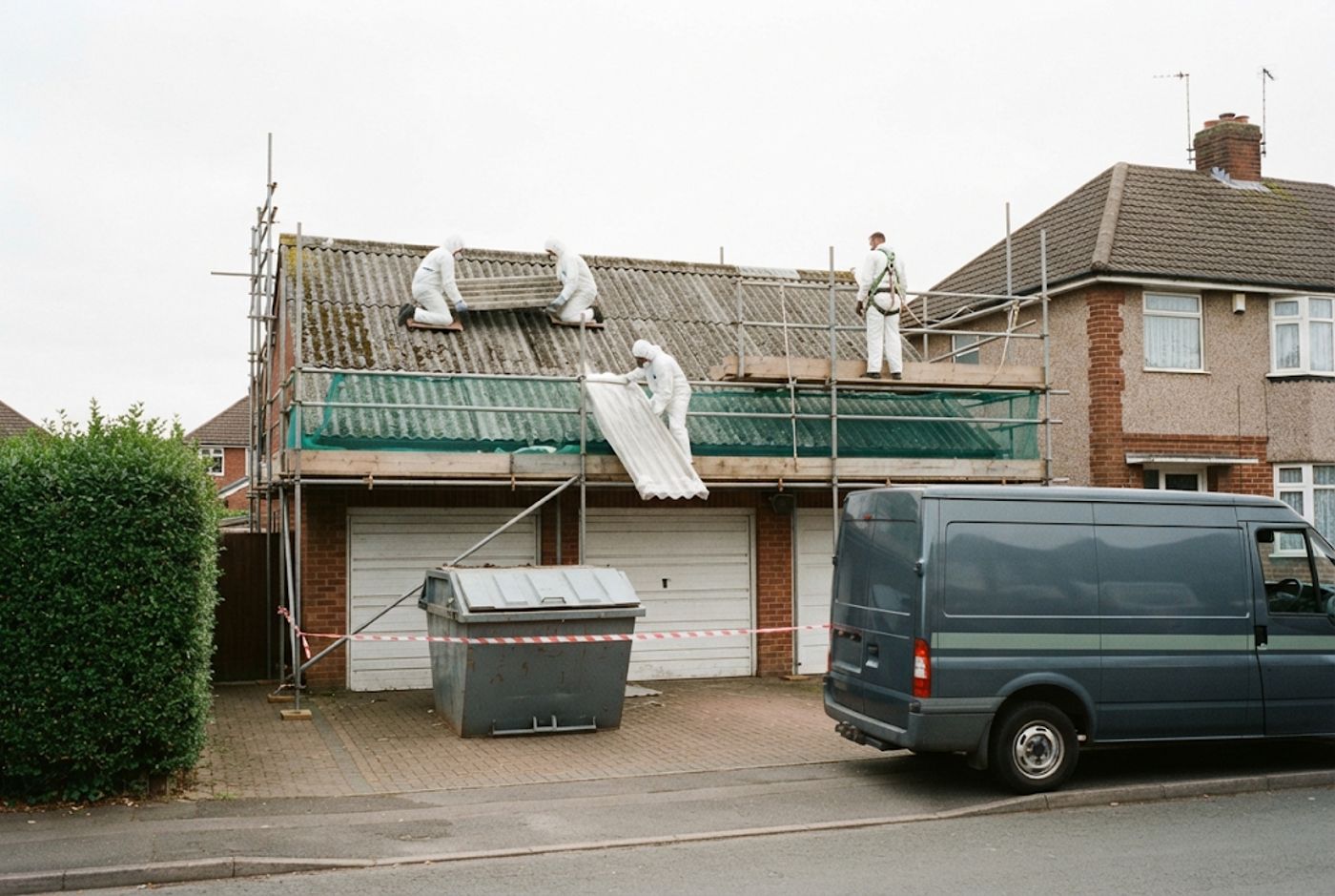 Scaffold up on a garage roof with a skip and van outside
